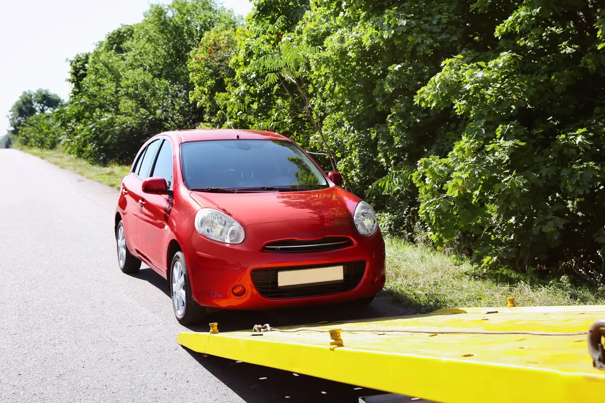 Red car ready to be loaded onto a yellow flatbed for vehicle transport